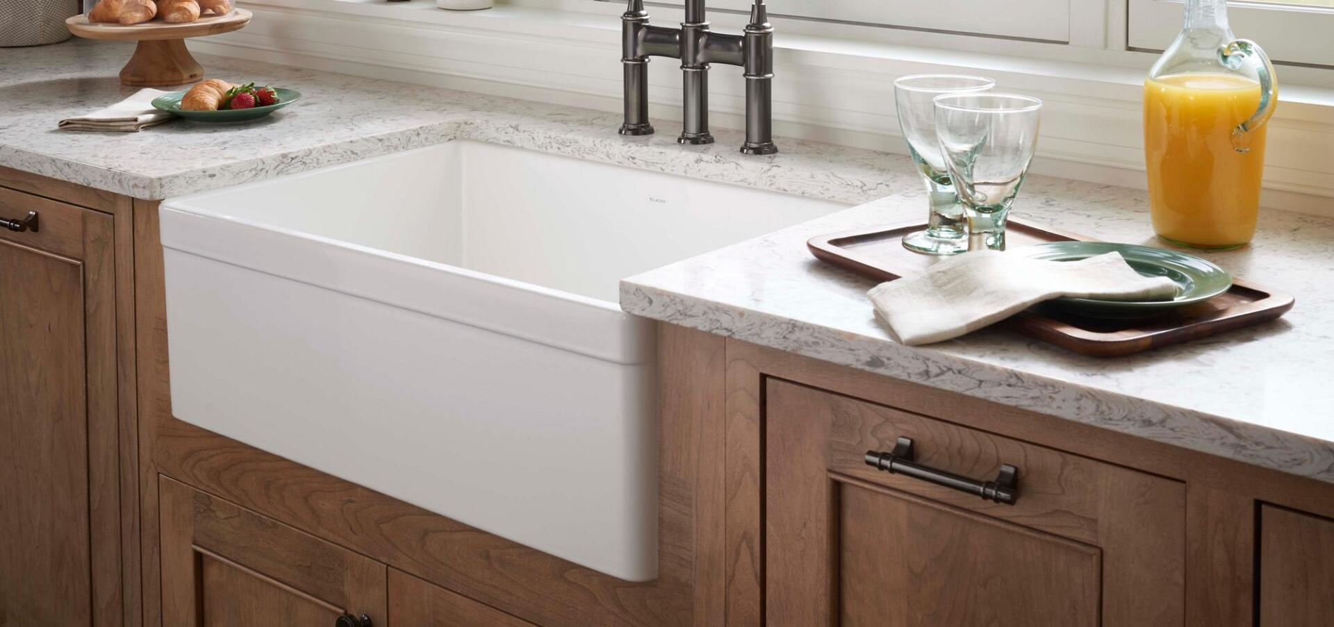 A kitchen sink with a glass of orange juice on the counter.