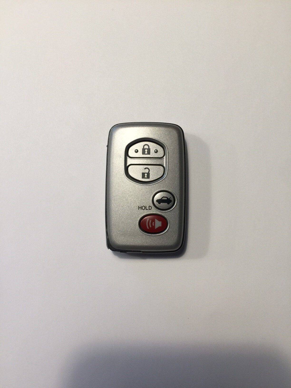 Silver car key fob with black buttons and a red panic button on a white background.