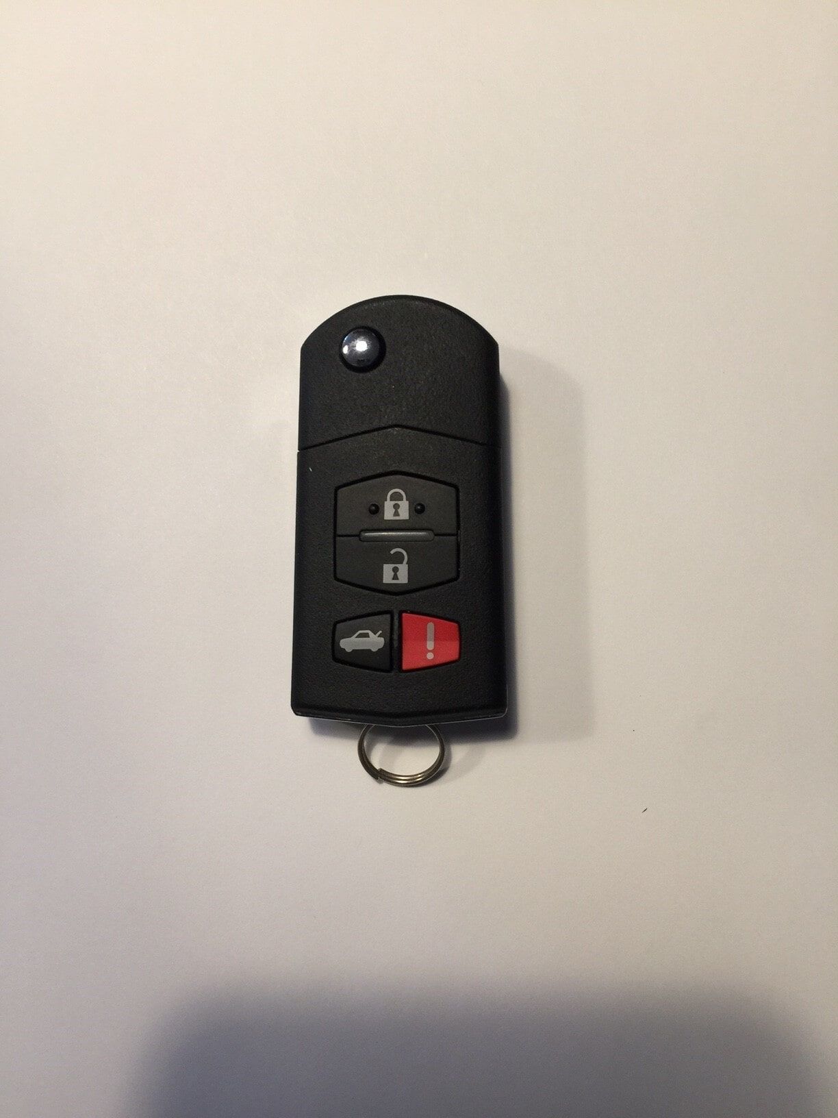 Black Mazda key fob with lock, unlock, and trunk buttons, on a white surface.