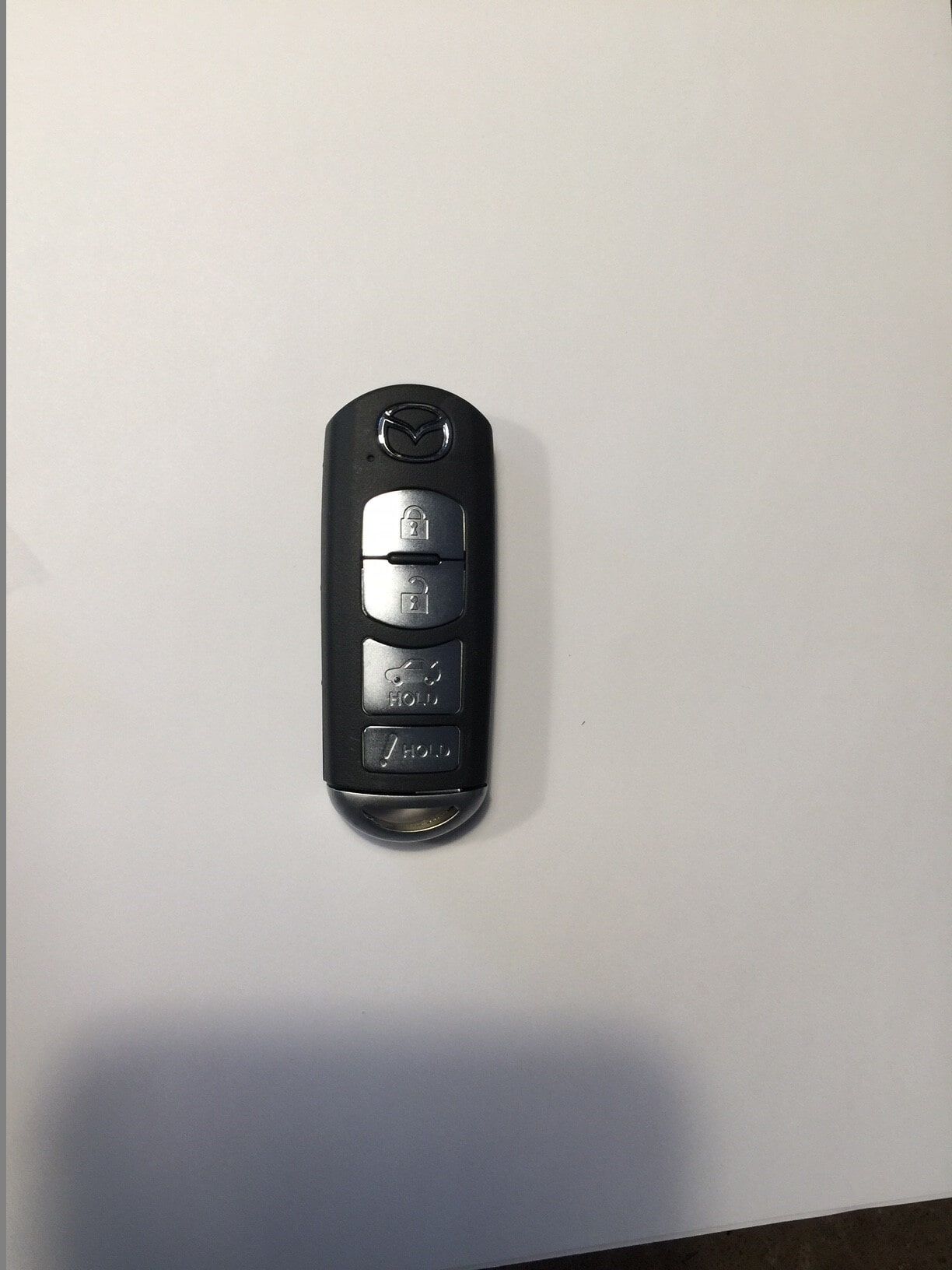 Black car key fob with three buttons on a white surface.