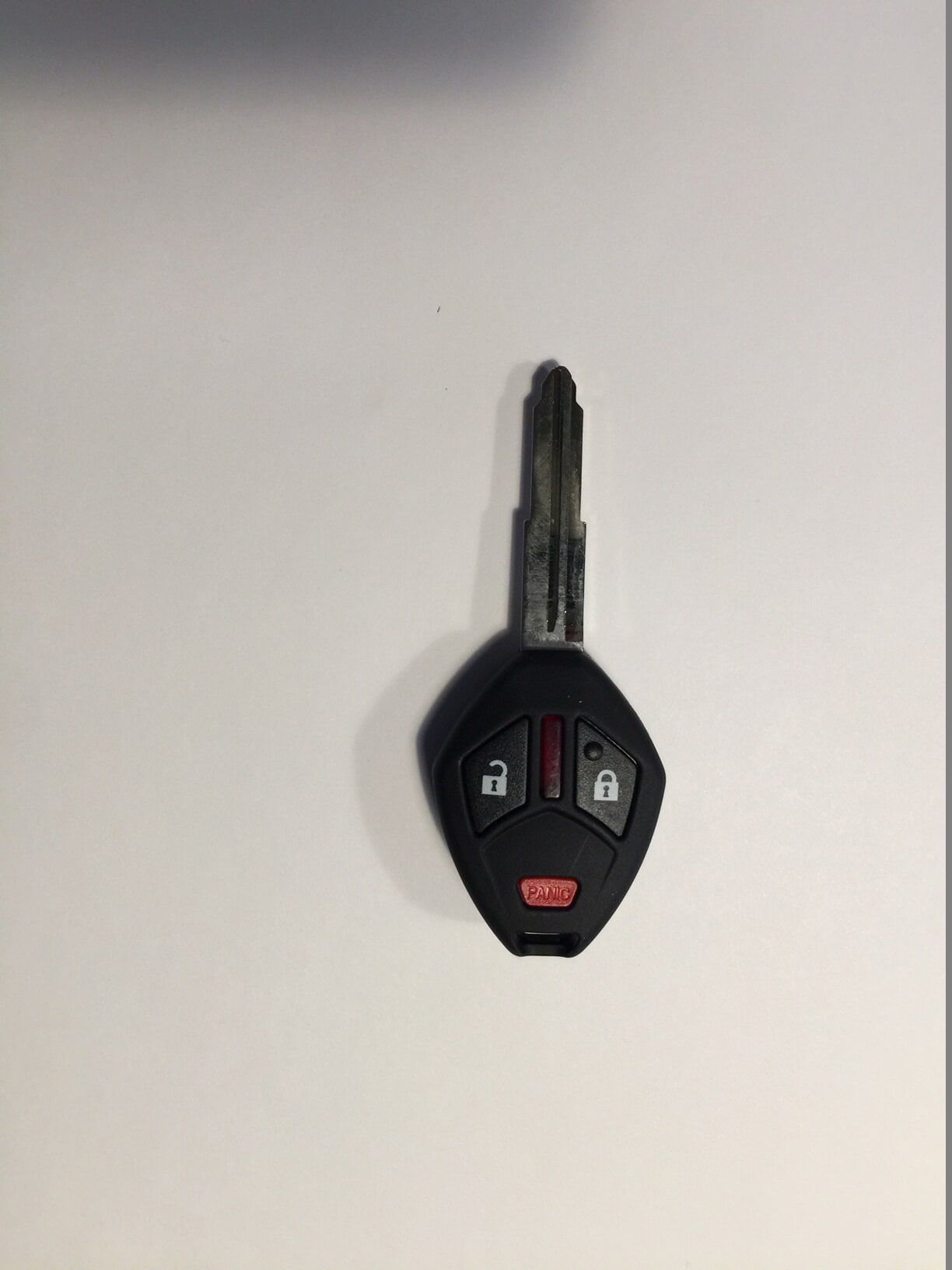 Black car key with remote control buttons on a white surface.