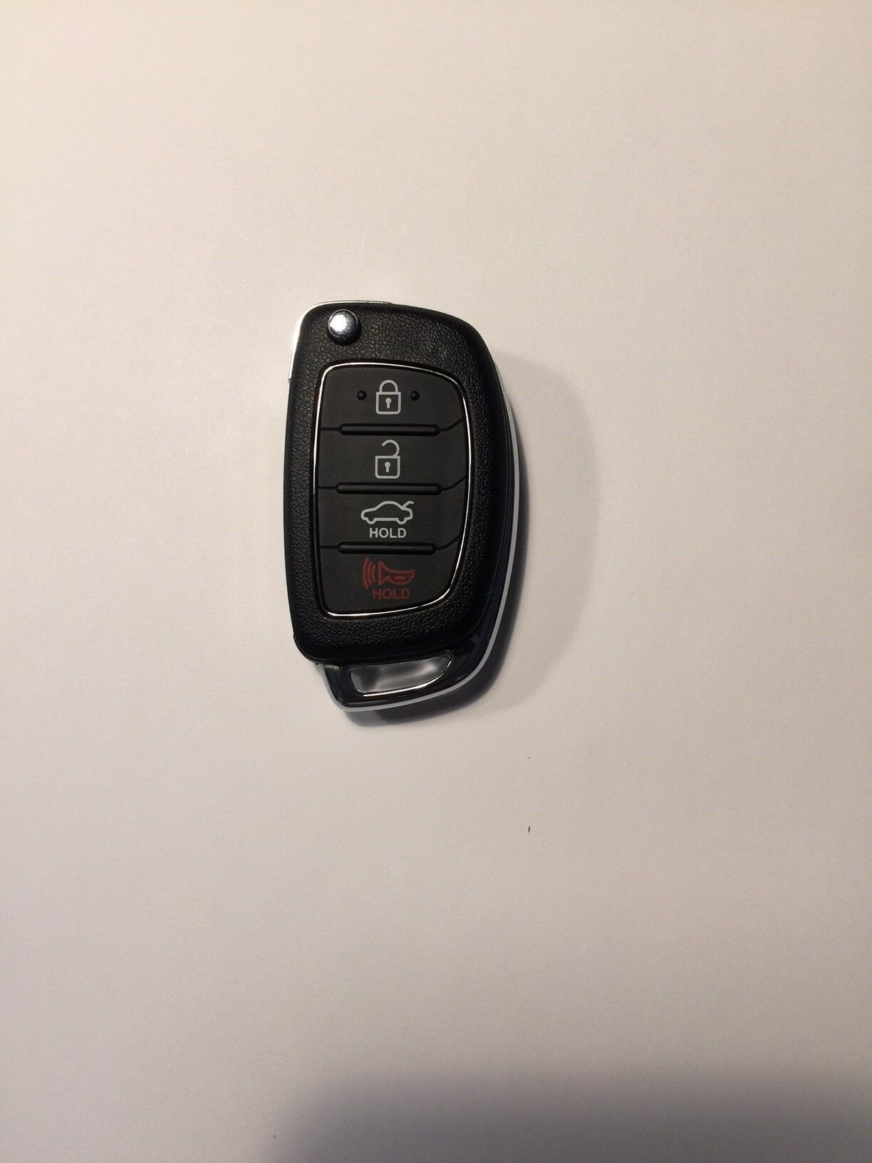 Black car key fob on a white surface; buttons for lock, unlock, trunk, and panic.
