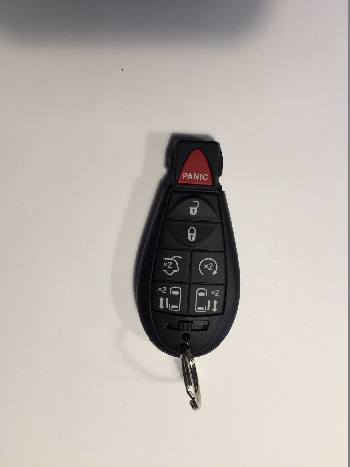 Black car key fob with buttons, a red panic button, and a silver key ring on a white surface.