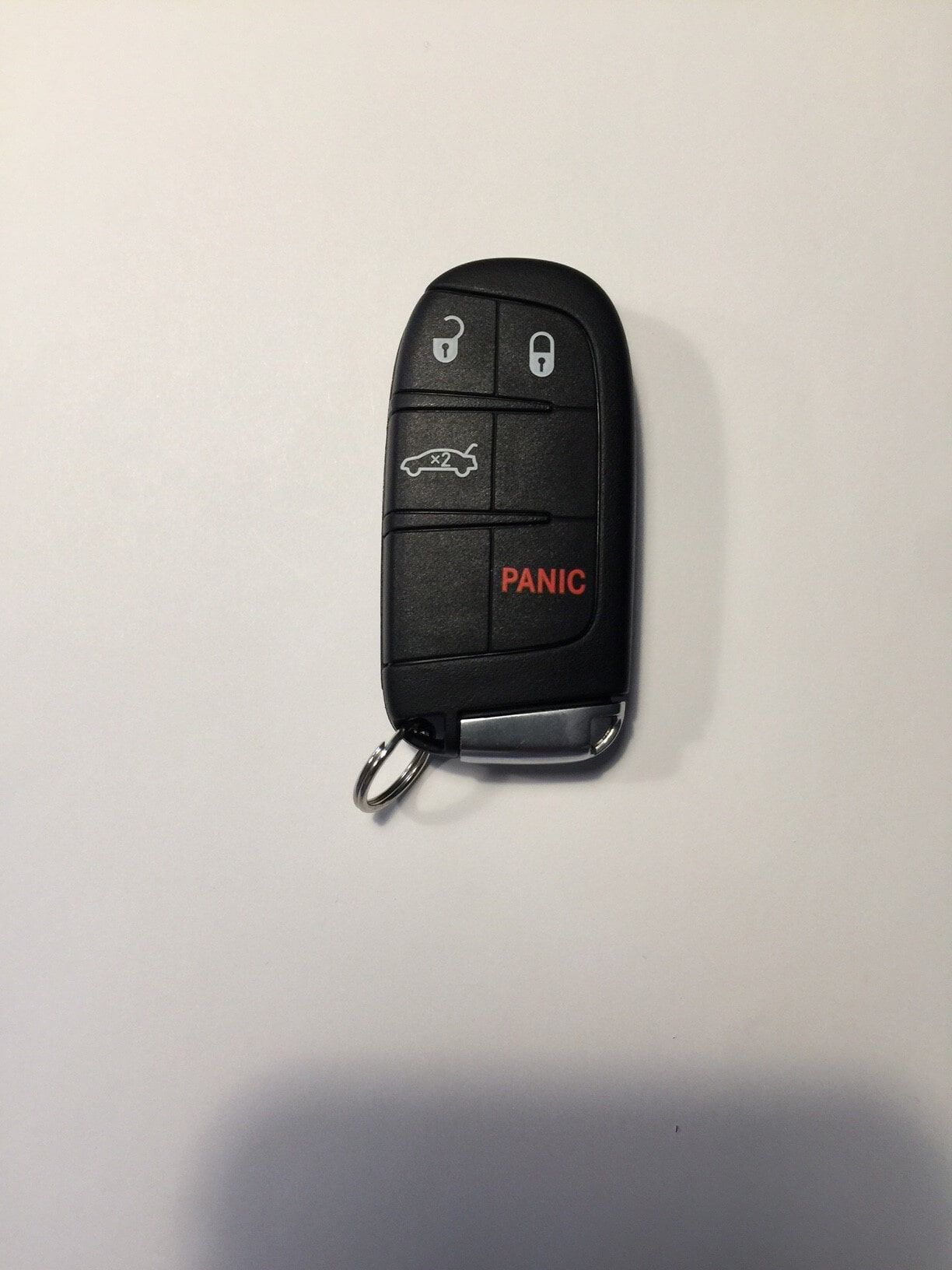 Black car key fob with keyless entry buttons and a red panic button, lying on a white surface.