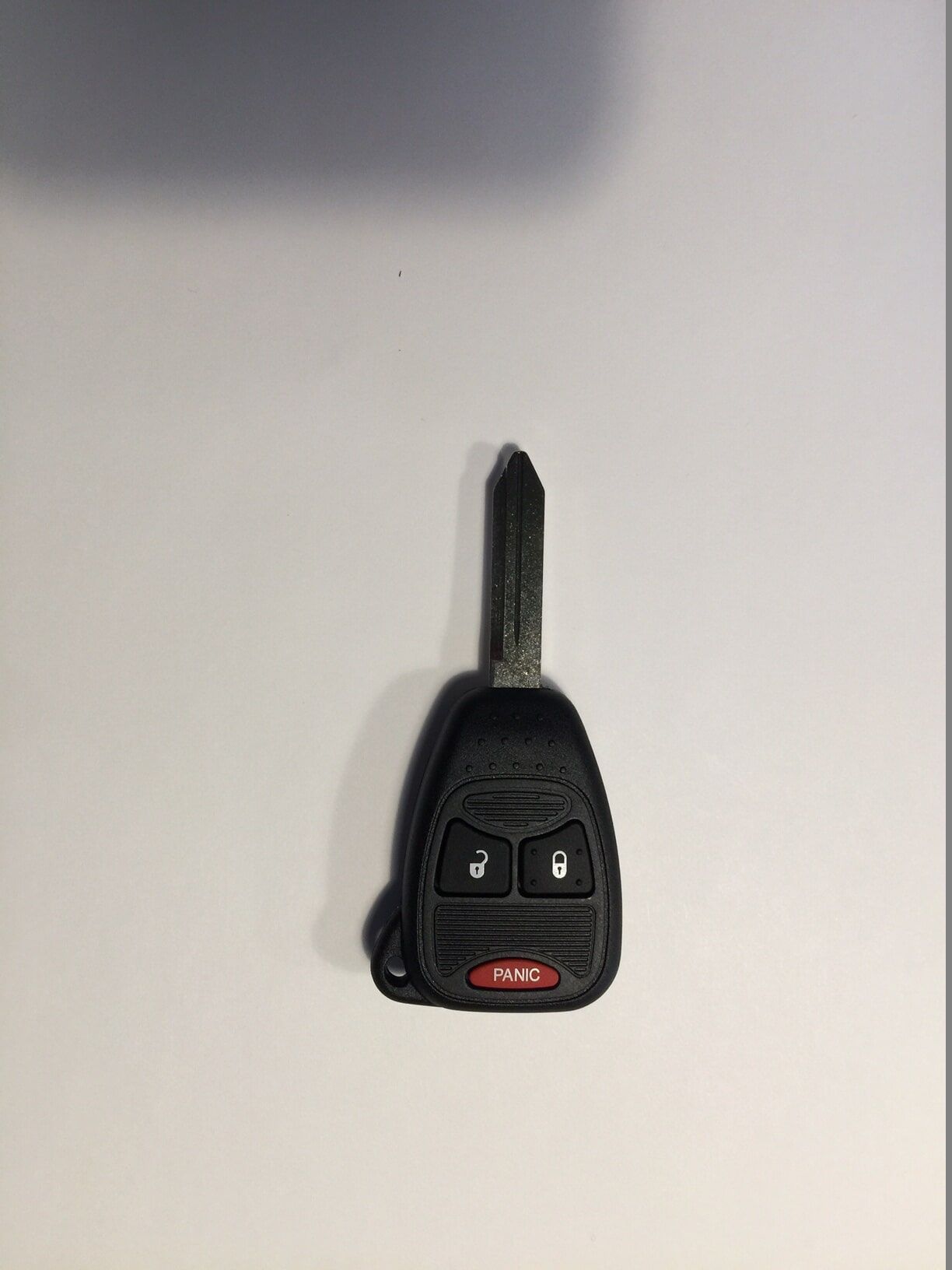Black car key with buttons and a metal blade on a white surface.