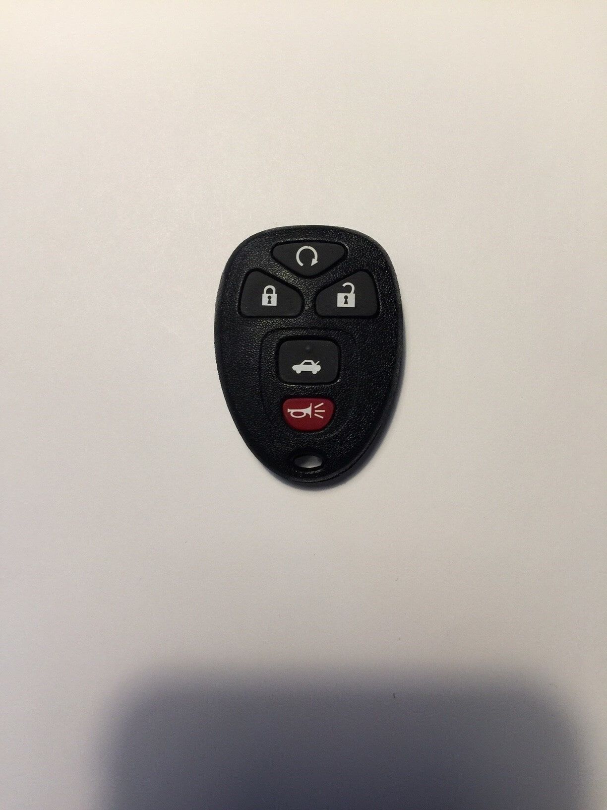Black car key fob with lock, unlock, panic, and trunk buttons on a white surface.