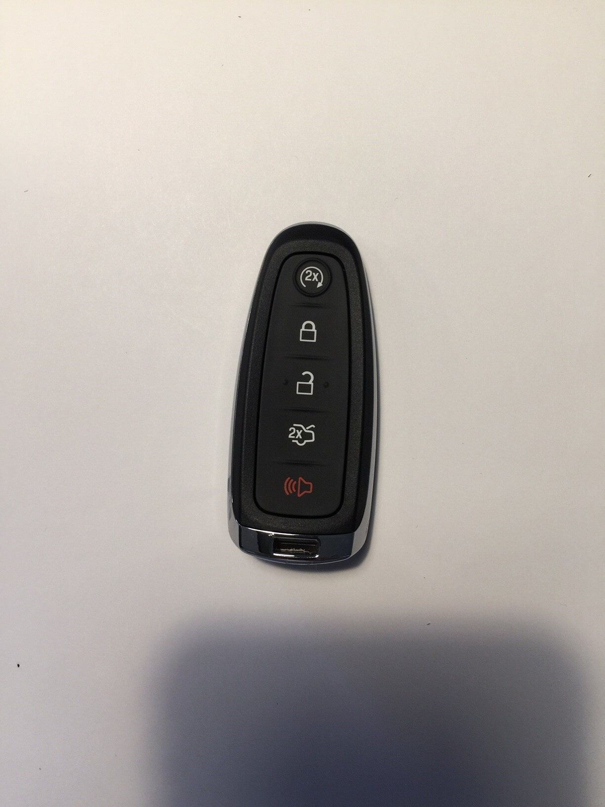 Black Ford key fob on a white surface; has buttons for lock, unlock, trunk, and panic.