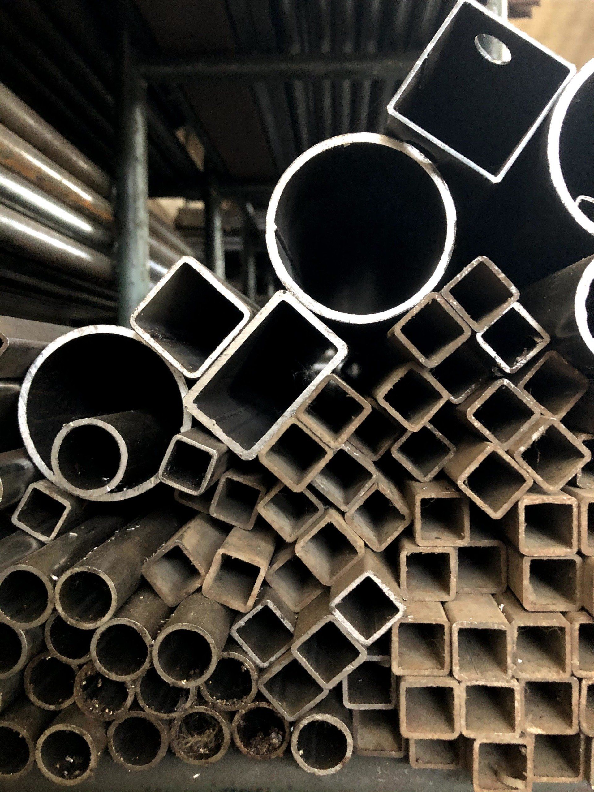 In un magazzino, si trova una scaffalatura piena di tubi metallici impilati di vario tipo e tubi quadrati cavi in ​​acciaio.