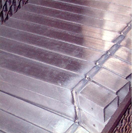 Una pila di tubi metallici rettangolari e lucidi, uniti tra loro da un'unica saldatura industriale continua.