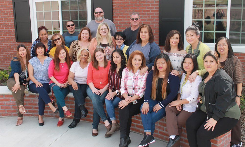Group of diverse people smiling while sitting on a brick ledge in front of a building.