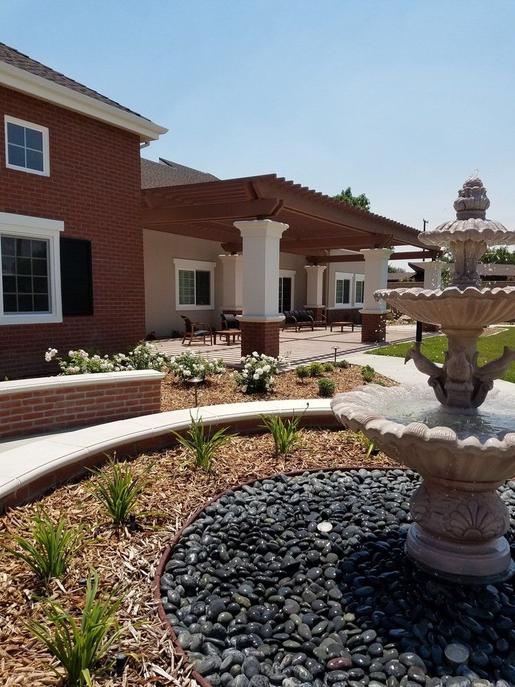 Exterior of a brick building with a pergola, a fountain, and garden beds filled with black rocks and plants.