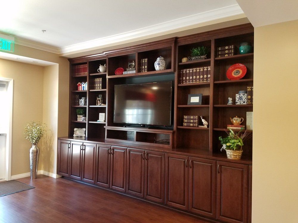 Built-in dark wood bookcase with TV, books, and decorations against a tan wall, a dark wood floor, and a doorway.