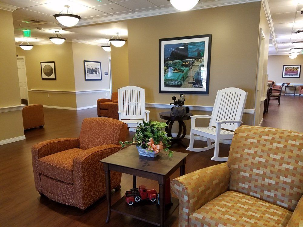 A senior living lounge with armchairs, rocking chairs, art, and lamps. The space has a welcoming, homey feel.