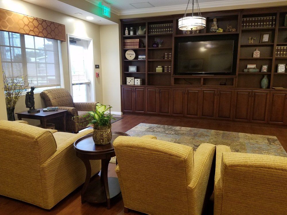 Cozy living room with built-in shelves, TV, and four yellow armchairs. Dark wood, neutral colors.