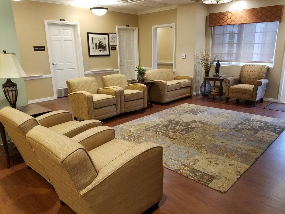 A comfortable lounge with beige chairs, a patterned rug, and a window with a patterned valance.