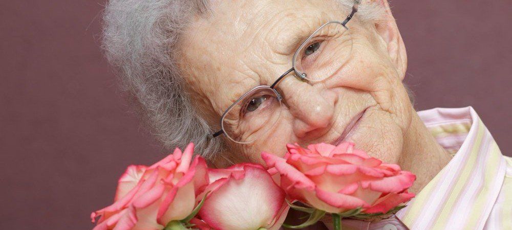 Elderly woman with glasses smells roses. Elderly woman smelling roses in Artesia, CA.