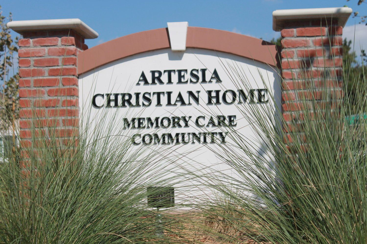 Sign for Artesia Christian Home, Memory Care Community. Red brick, white background, tan arch, lettering.