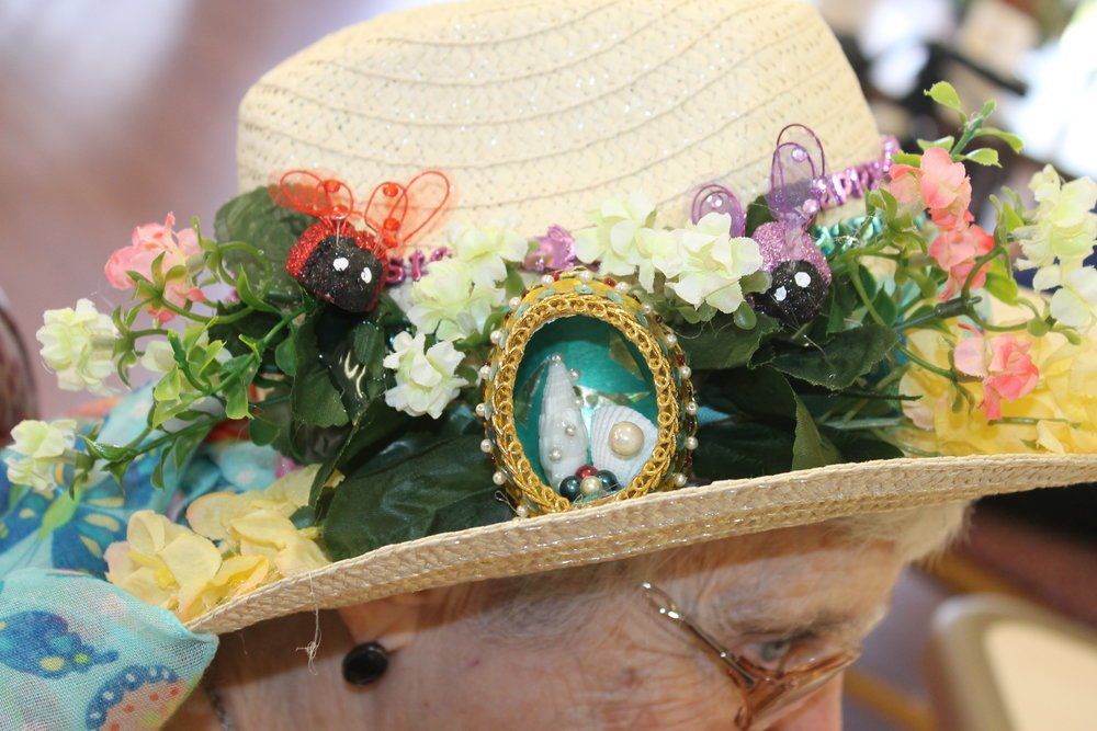 Woman wearing a decorated straw hat with flowers, bugs, and a framed sailboat.