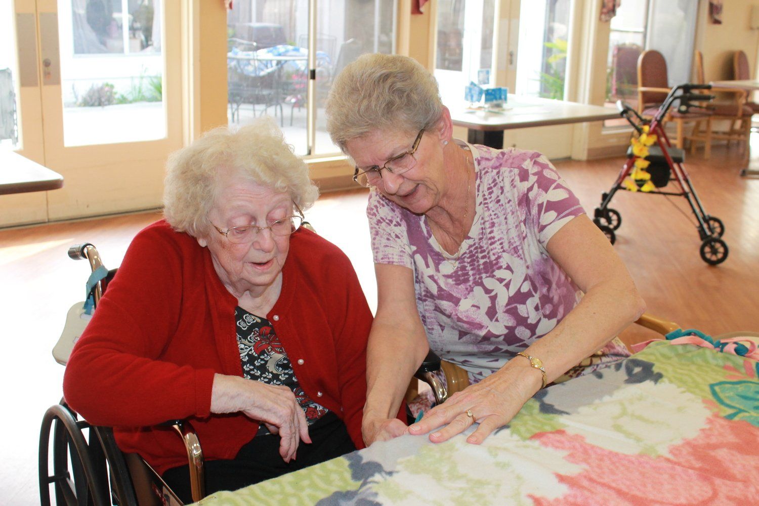 Woman in wheelchair looks at quilt with another woman in a brightly lit room.