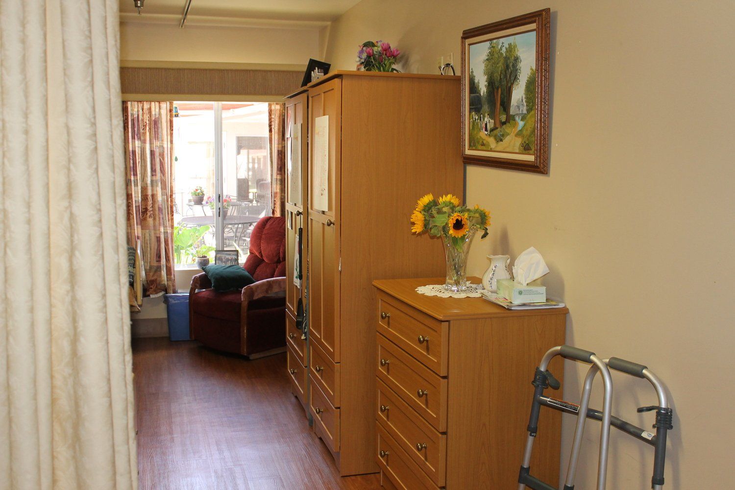 Hallway in a senior living space, brown wood furniture, painting, flowers, walker.