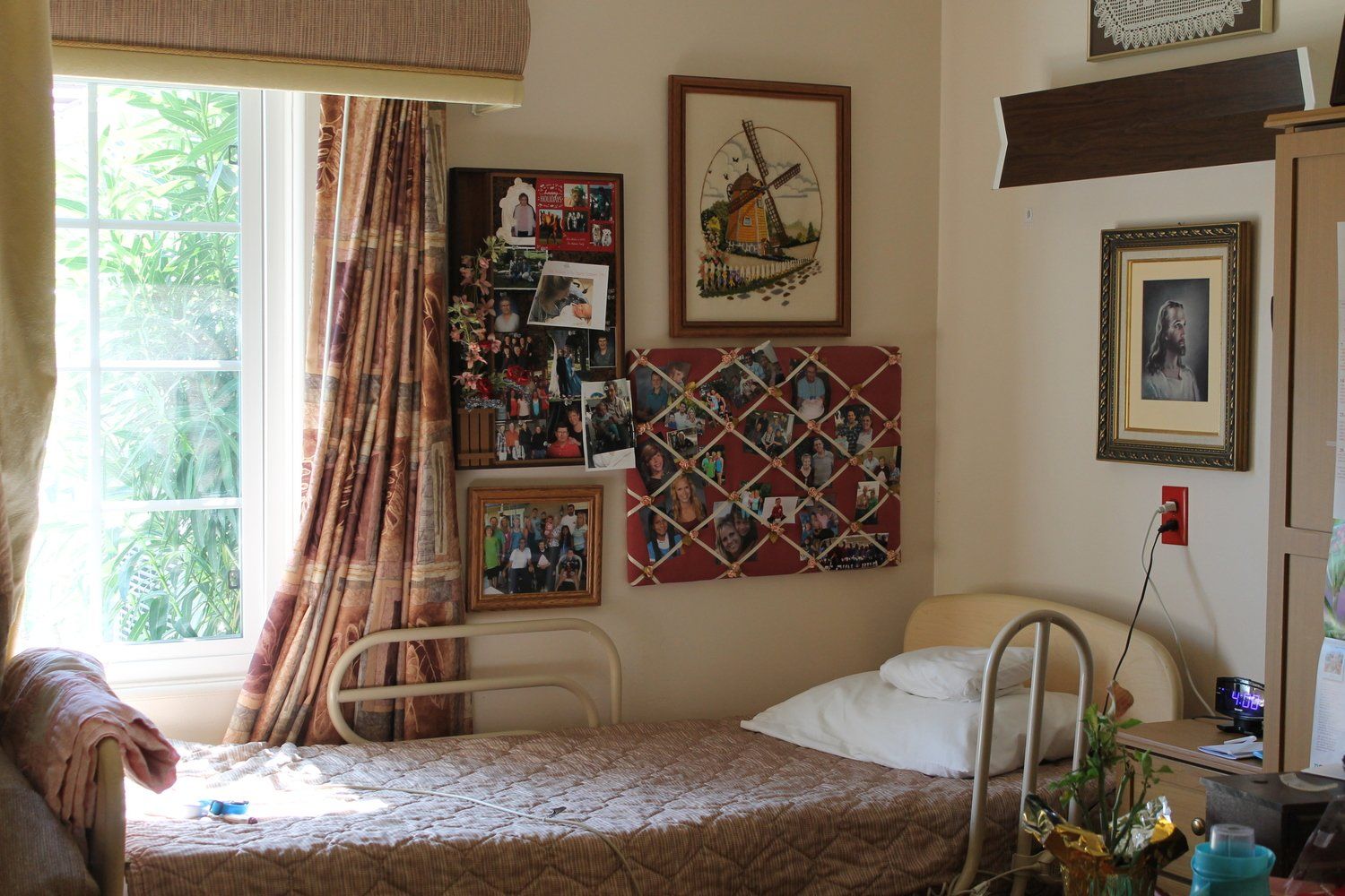 Bedroom with bed, window, framed photos, and corkboards. Sunlight illuminates the space.