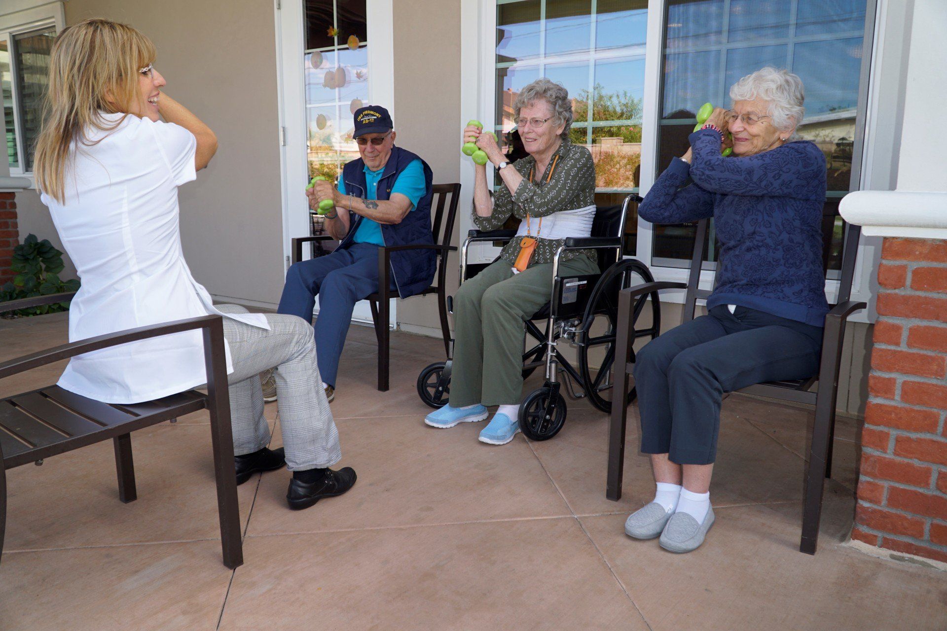 A blonde woman leads seated senior citizens in a workout outdoors.