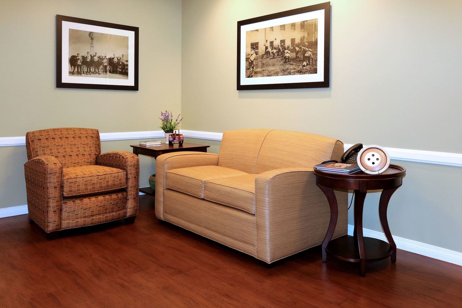 Cozy waiting area with loveseat, chair, and end tables. Two framed photos on the wall, wooden floor.