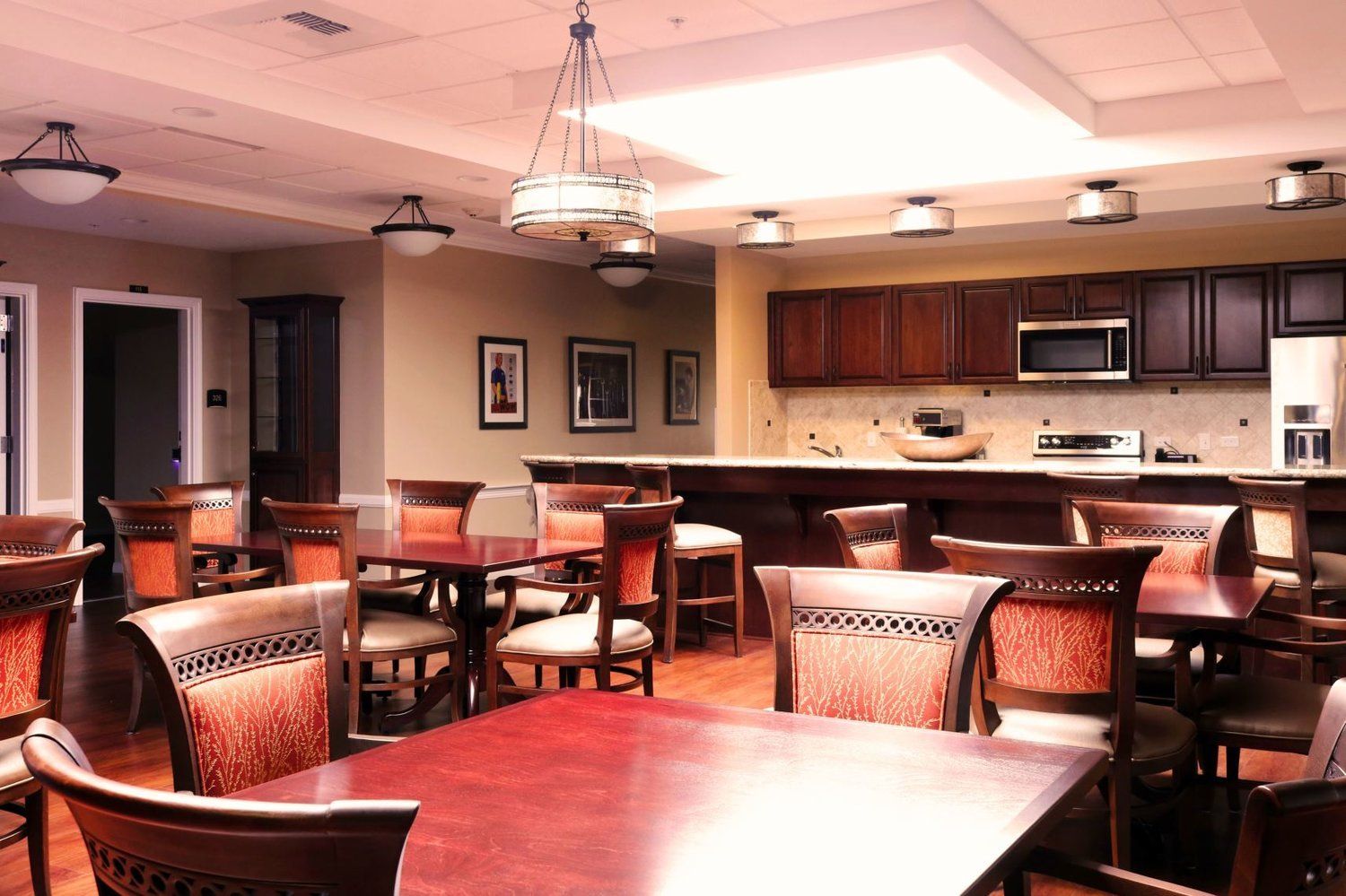Dining area with square tables and chairs, dark wood cabinets, and a small kitchen.