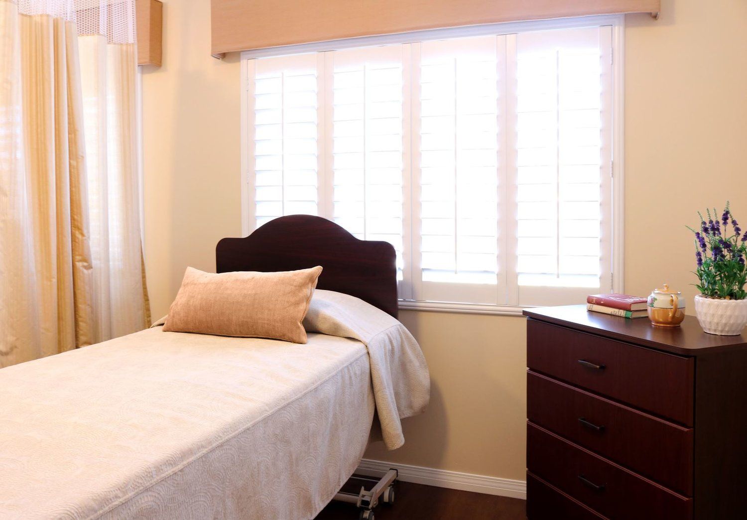 Bedroom with a single bed, dresser, and window with white shutters; beige walls.