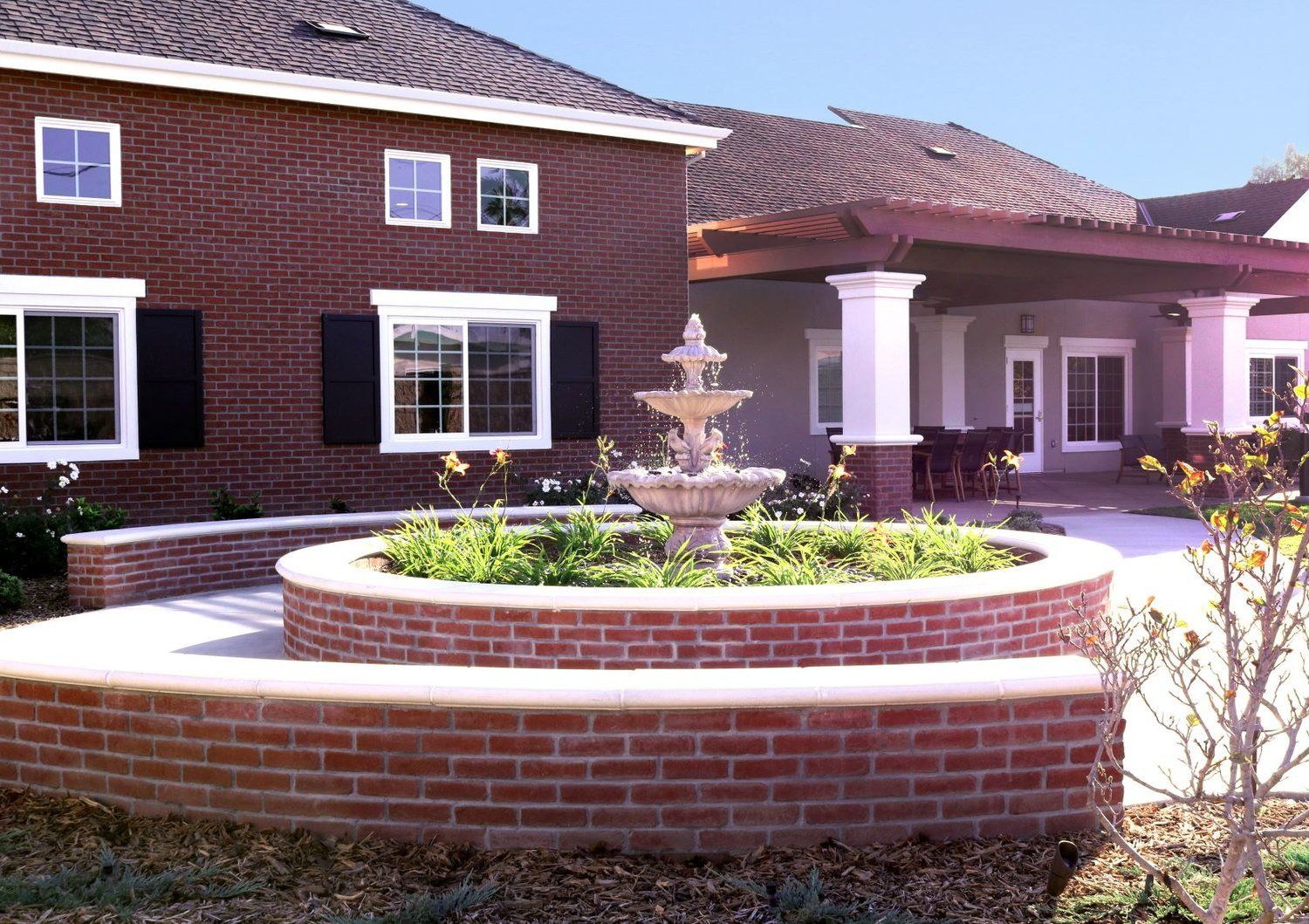 Red brick building with fountain, surrounded by greenery.