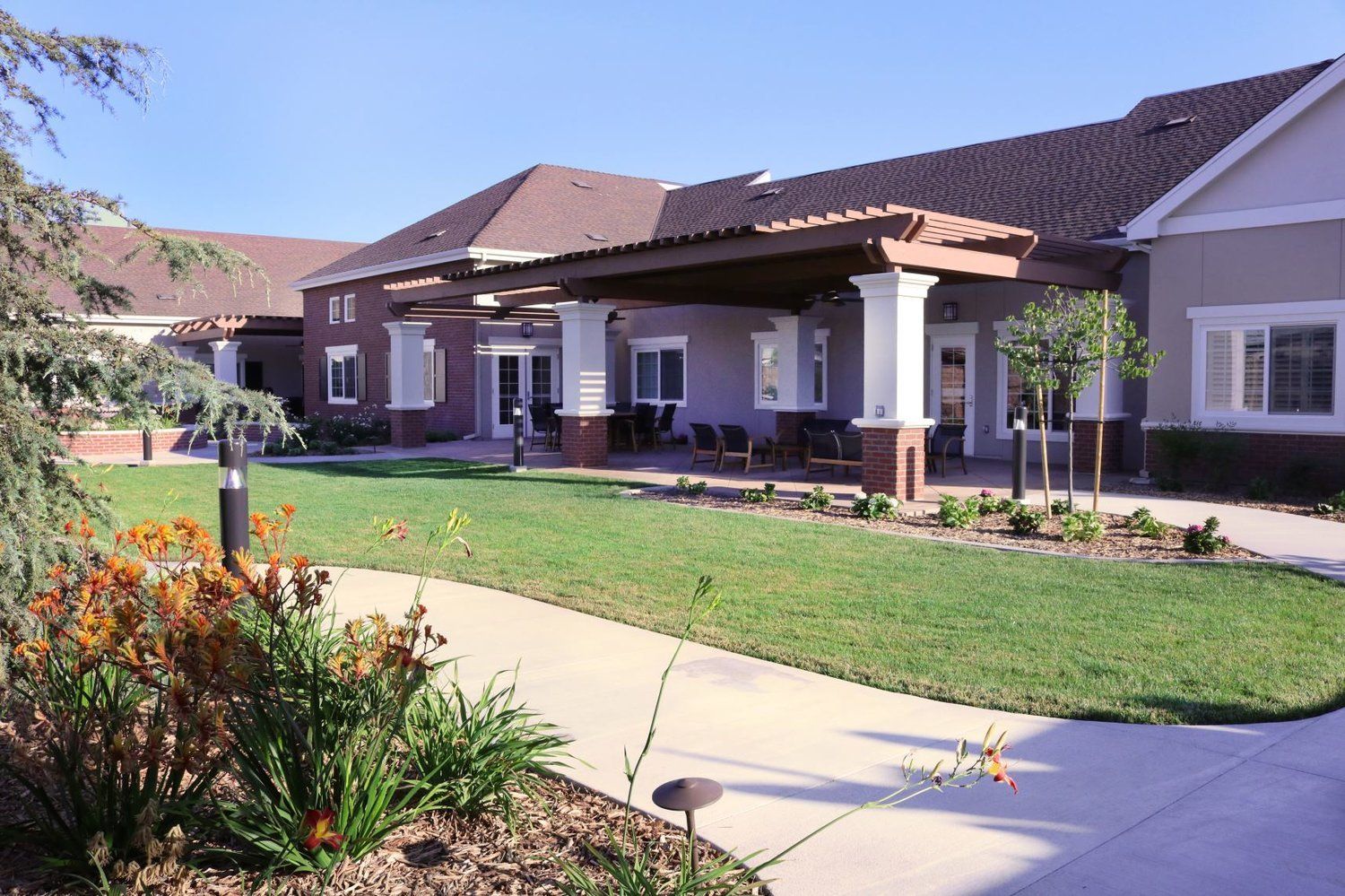 Exterior view of a senior living facility with a covered patio, green lawn, and landscaping.