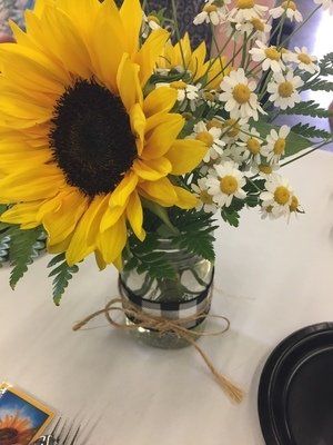 Sunflower and daisies in a jar, decorated with black and white ribbon and twine on a white table.