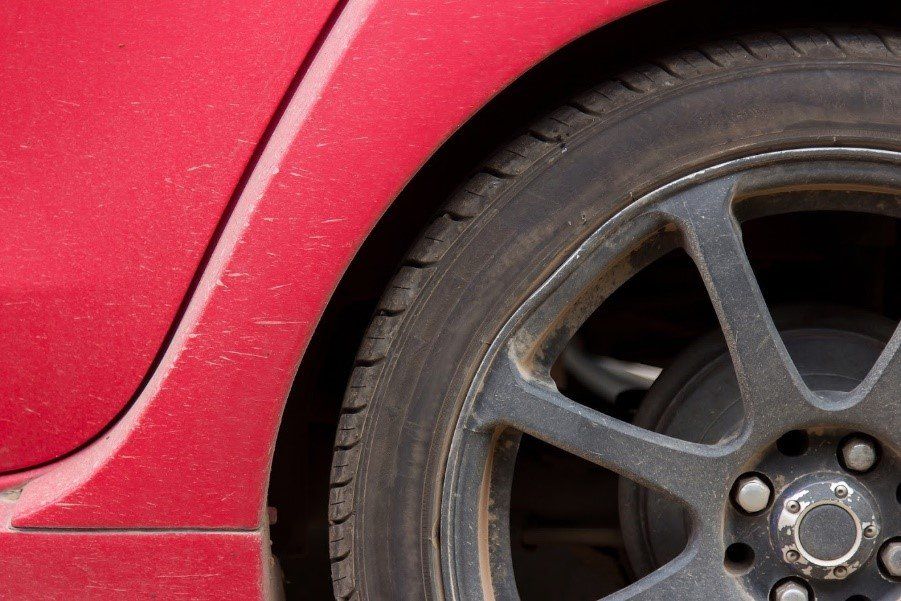 Red car body and dirty black tire.