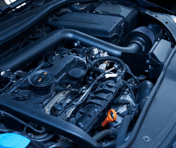 Car engine with black plastic components and orange fluid cap.