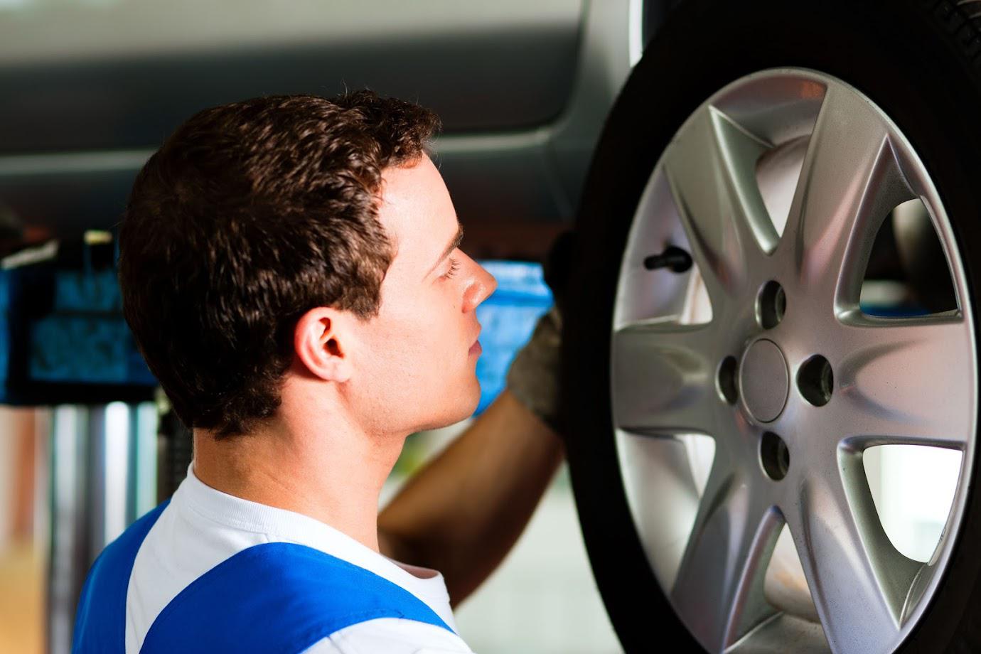 Mechanic inspecting a car tire in a garage, looking at the wheel rim.