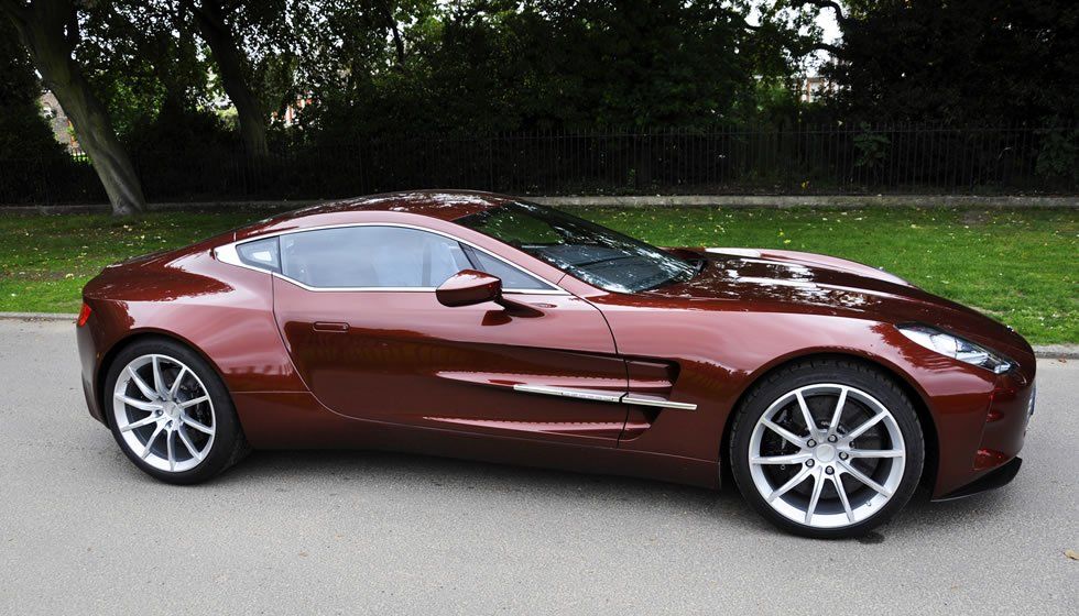 Brown Aston Martin sports car parked on a paved road, daytime.