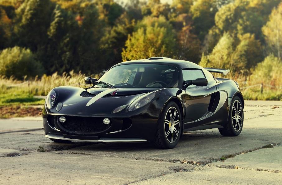 Black Lotus sports car parked on asphalt, trees in background.