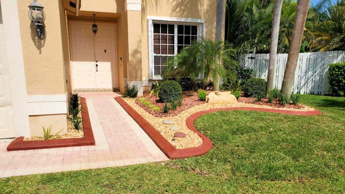 Front yard landscaping with brick pathway, green lawn, and beige house.