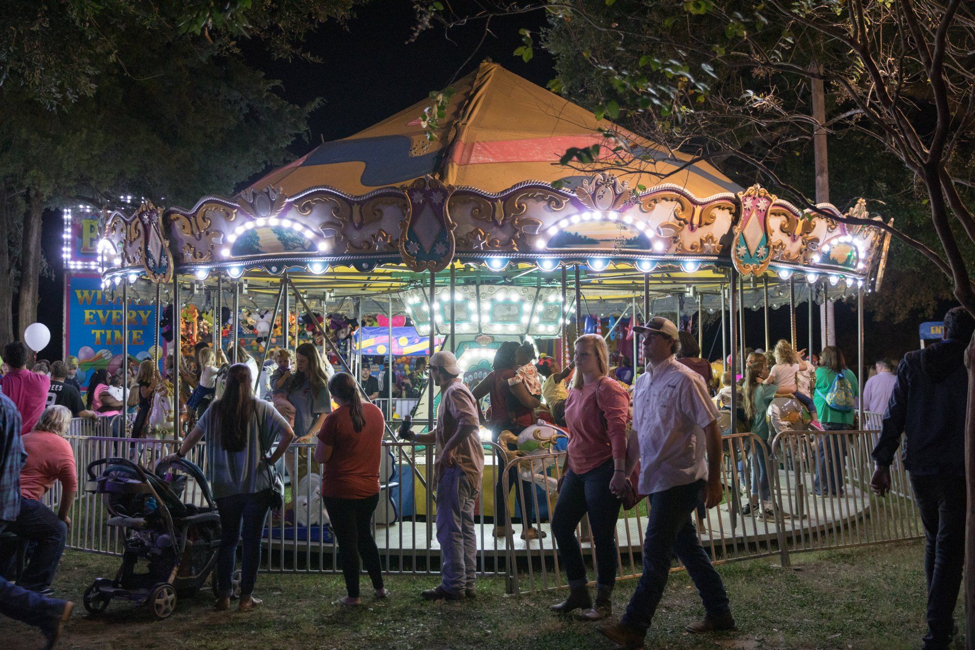 A group of people are standing around a merry go round at night.