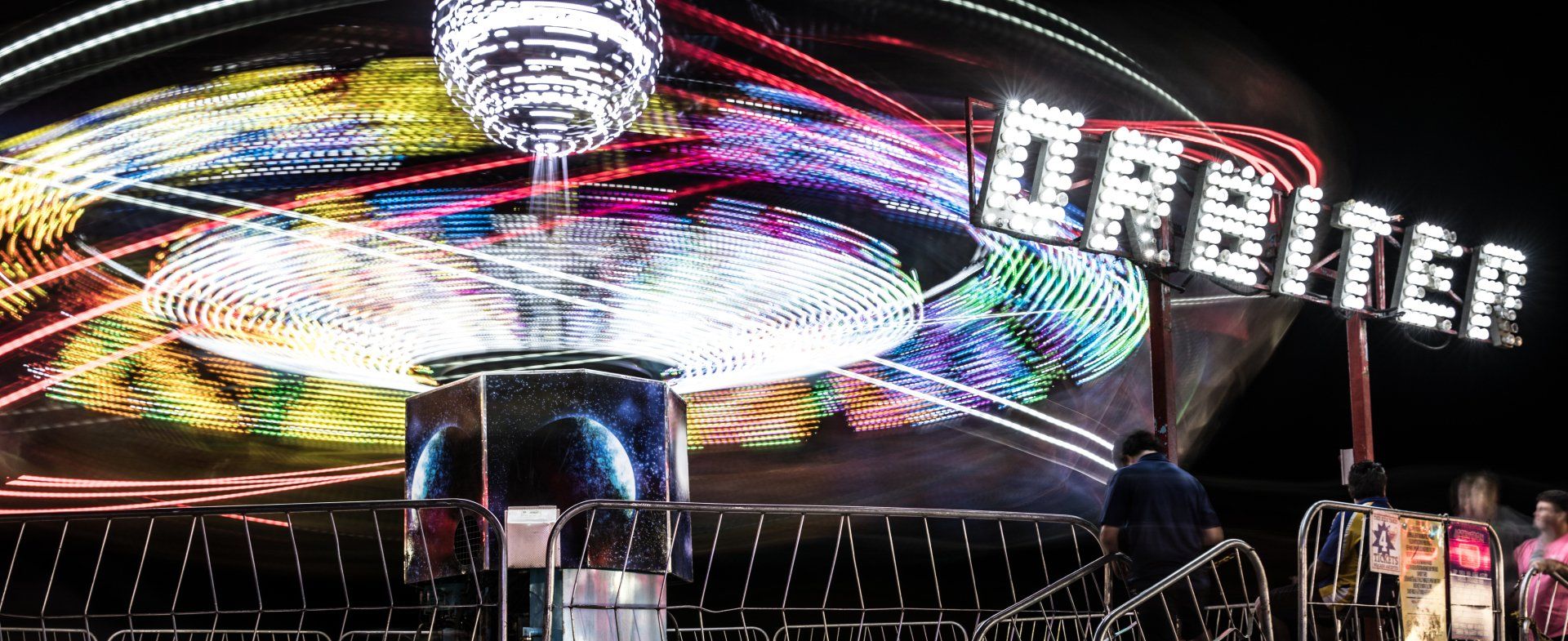A carnival ride called orbiter is lit up at night.