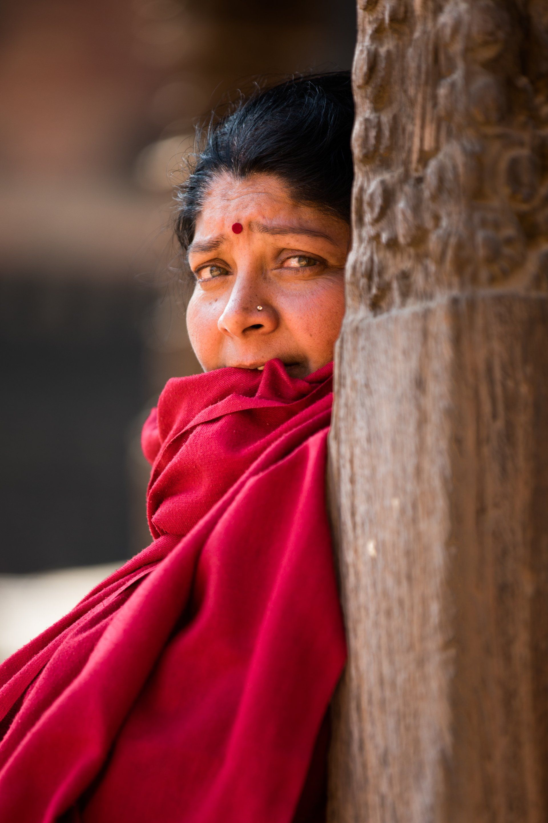 A woman in a red scarf is leaning against a wooden post.