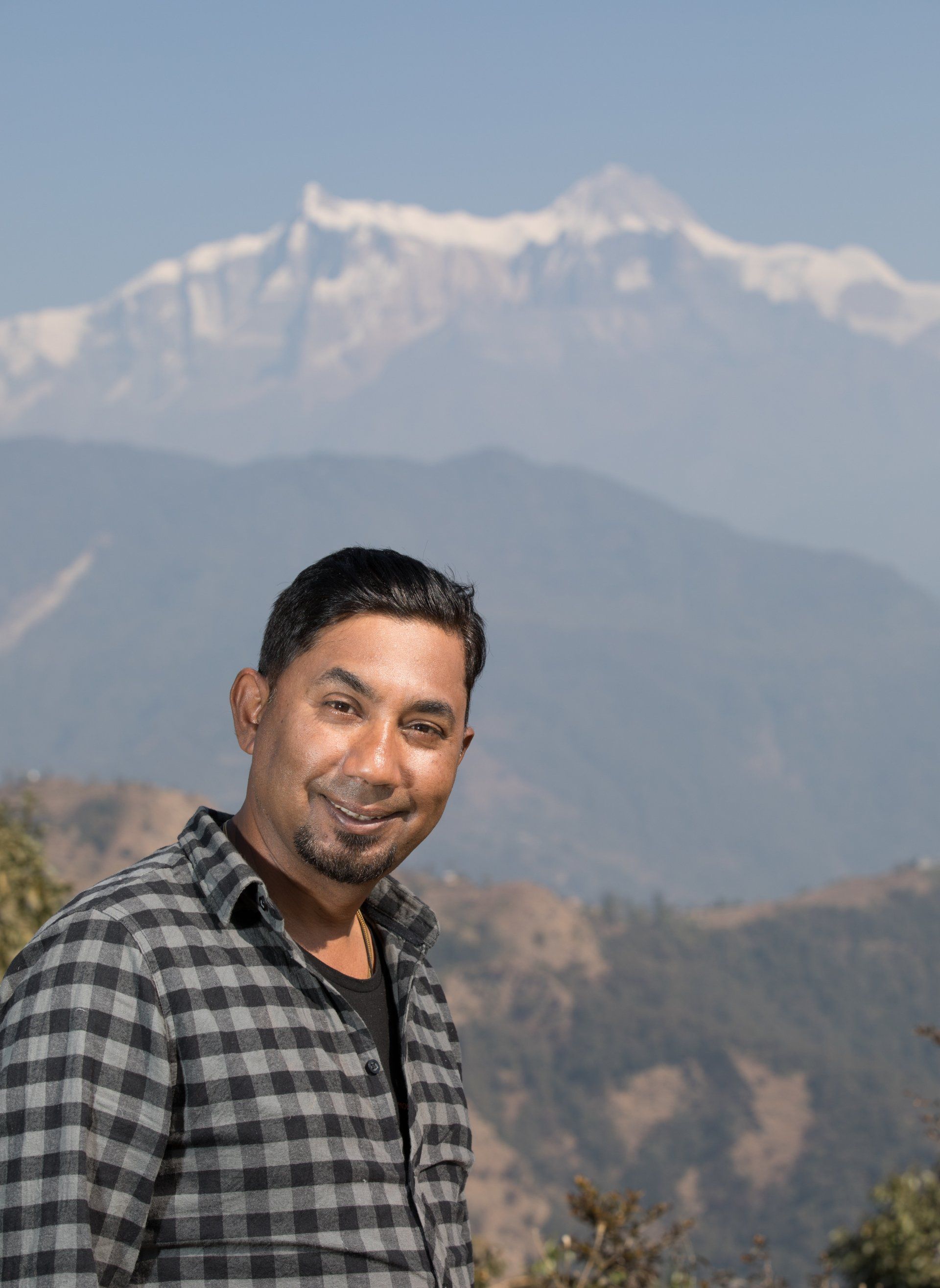 A man in a plaid shirt is standing in front of a mountain.