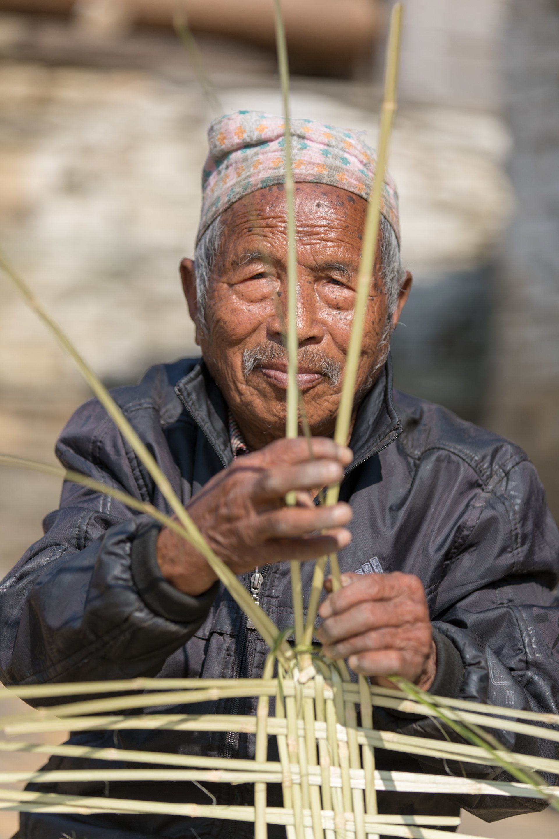An elderly man is weaving a basket out of bamboo.