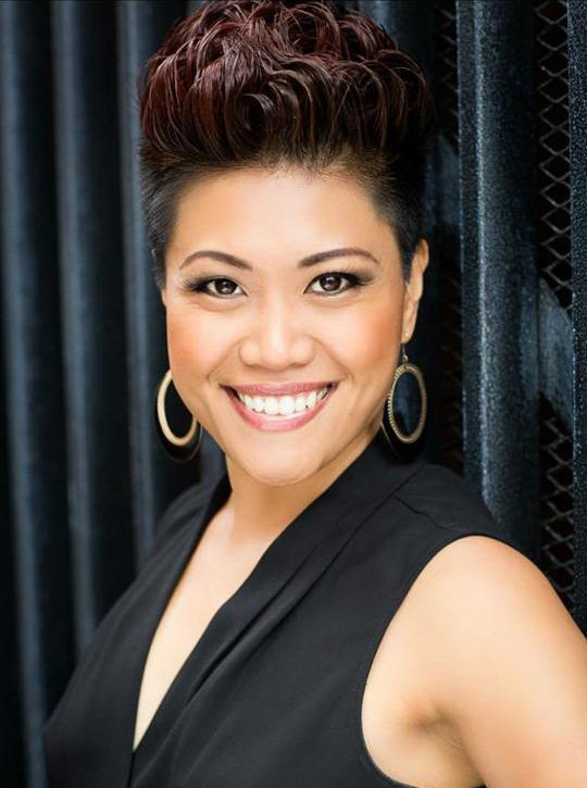 A woman with short hair is smiling and wearing earrings