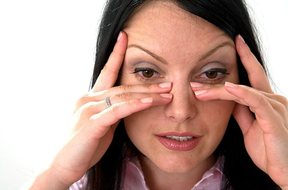 A woman is rubbing her nose because she has a headache.