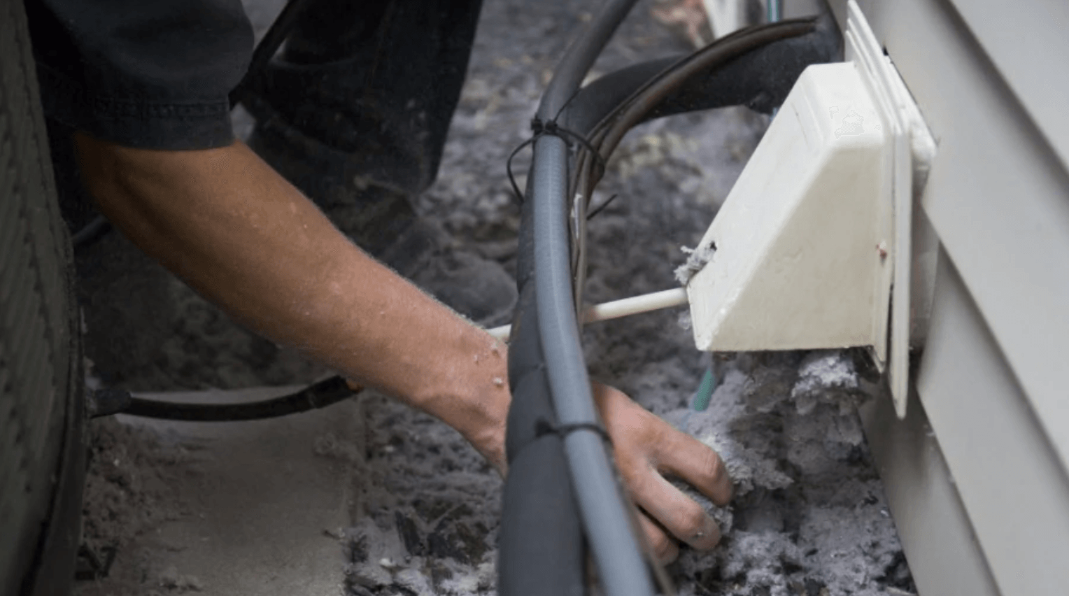 A person is working on an electrical outlet on the side of a house.