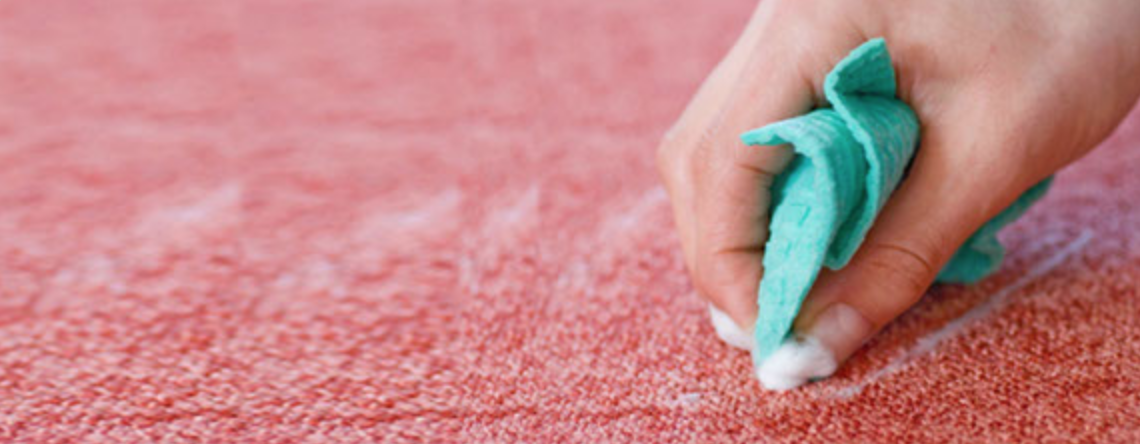 A person is cleaning a pink carpet with a green cloth.