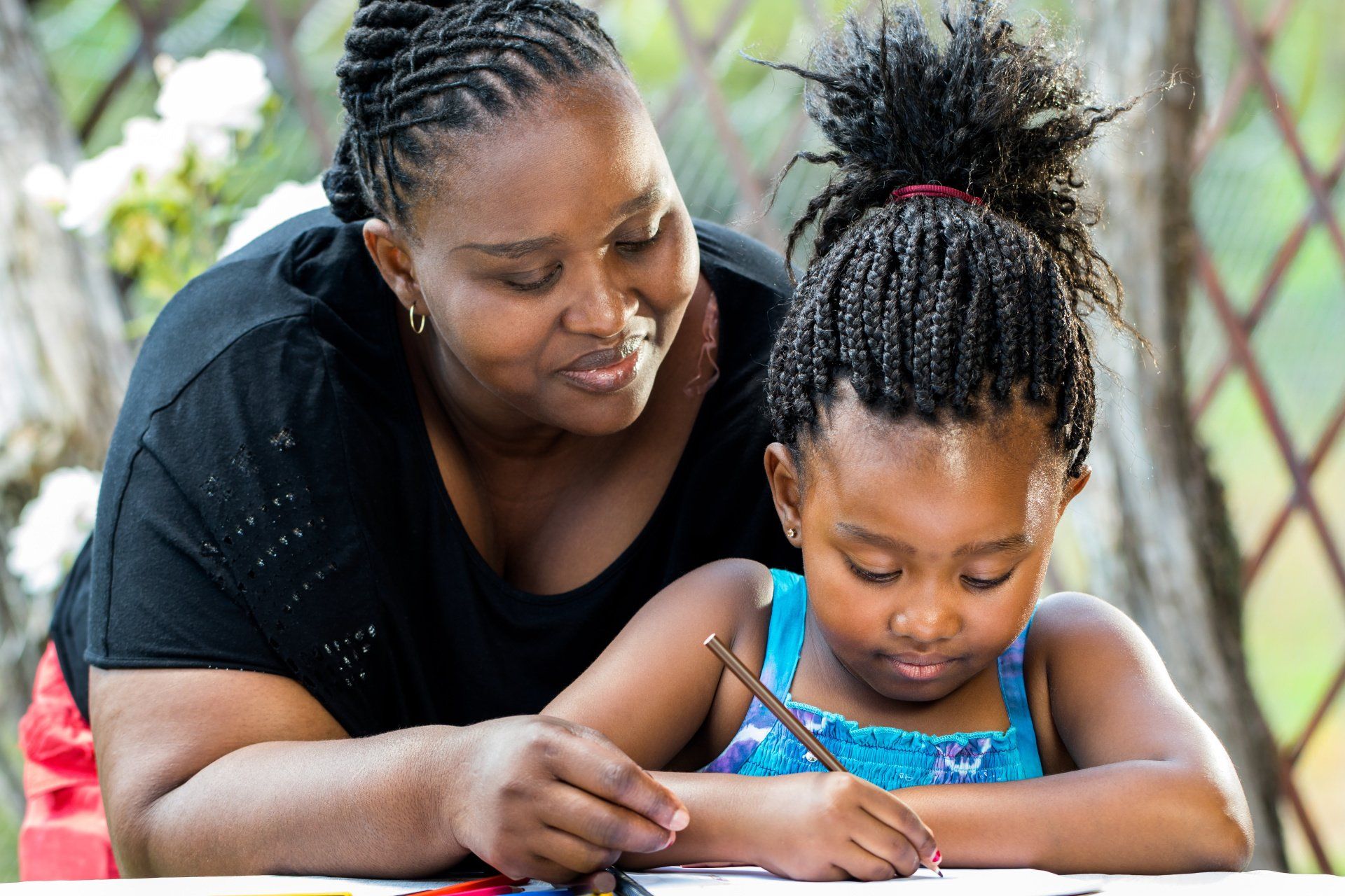Woman helping child write outdoors.