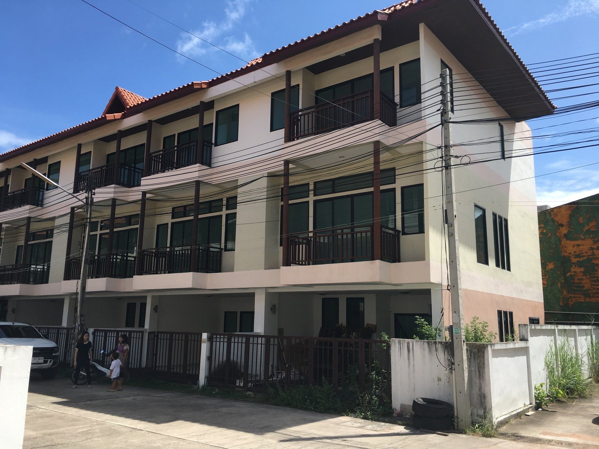 Multi-story townhouses with balconies, off-white walls, brown trim, under a blue sky.