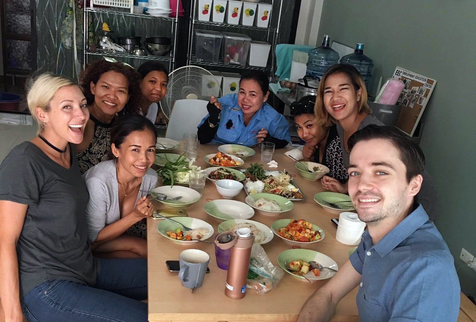 People smiling around a table with food, in a bright room.